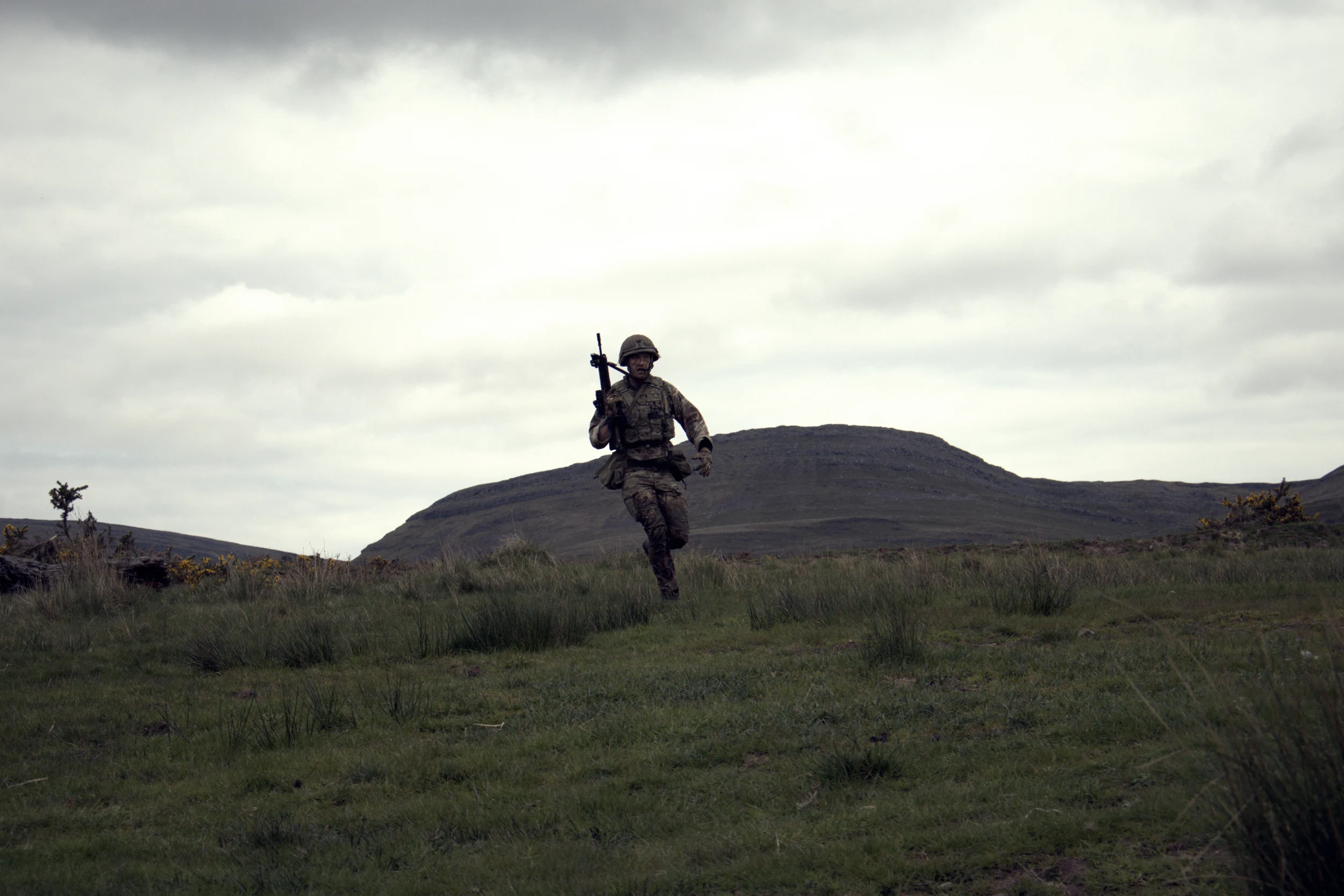 A soldier crossing open moorland beneath a dramatic sky