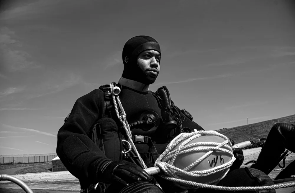Diver in a wetsuit holding coiled rope aboard a boat